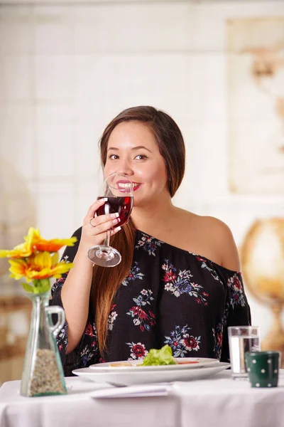 Porträt einer schönen eleganten Frau mit langen Haaren, die allein einen Rotwein in einem Restaurant vor verschwommenem Hintergrund trinkt — Stockfoto