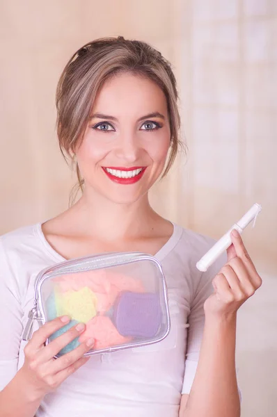 Primo piano di una giovane bella donna sorridente che tiene in mano un tampone di cotone mestruale e una borsa colorata locanda l'altra mano, su uno sfondo sfocato — Foto Stock