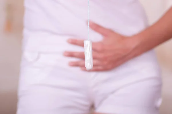 Jonge vrouw houden een menstruatie katoen tampon met haar hand en zetten voor haar witte korte — Stockfoto