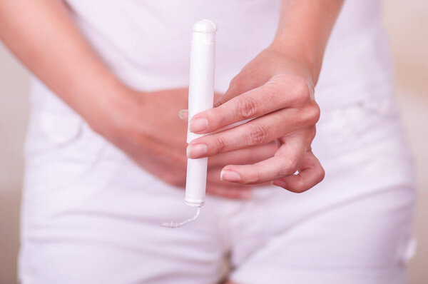 Молодая женщина с менструацией тампона хлопка с рукой и положить перед ней белый короткий
