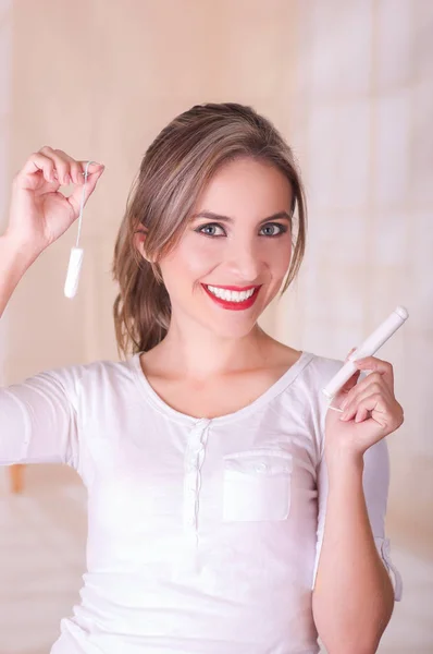 Joven hermosa mujer sonriente sosteniendo dos tampones de algodón de menstruación en un fondo borroso — Foto de Stock