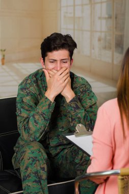 Yakışıklı genç giyen üniforma ile ağzını her iki elinizi kullanarak ve savaş, bir ofiste dehşetini hatırlayarak kapsayan bir kadın terapist bir tıbbi sağlık merkezinde stres acı asker