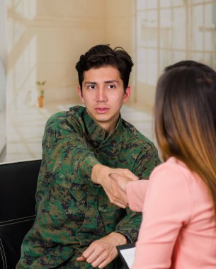 Yakışıklı genç asker üniforması, office arka planda bir tıbbi sağlık merkezinde tedavi için el sıkışan bir kadın terapist ile