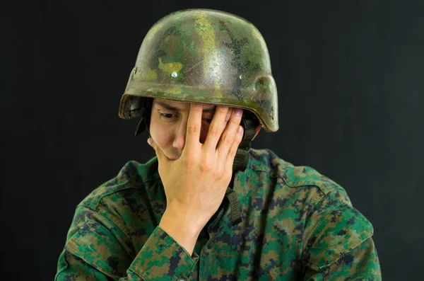 Красивый грустный молодой солдат в униформе страдает от стресса, закрывая лицо рукой, на черном фоне. — стоковое фото