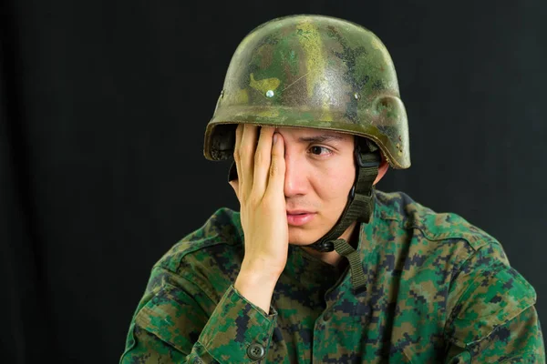 Krásný smutný mladý voják nosí uniformu trpí stresem s rukou, zakrývaje si tvář, v černém pozadí — Stock fotografie