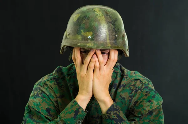 Guapo joven soldado vestido de uniforme que sufre de estrés, usando ambas manos para cubrir su cara, en un fondo negro — Foto de Stock