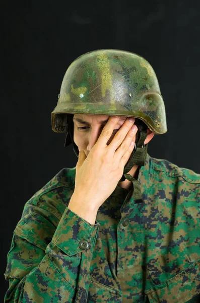Guapo joven soldado vestido de uniforme que sufre de estrés con la mano cubriendo su cara, en un fondo negro —  Fotos de Stock