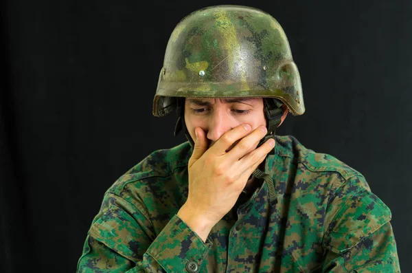 Guapo joven soldado vestido de uniforme que sufre de estrés con la mano cubriendo su boca, en un fondo negro —  Fotos de Stock