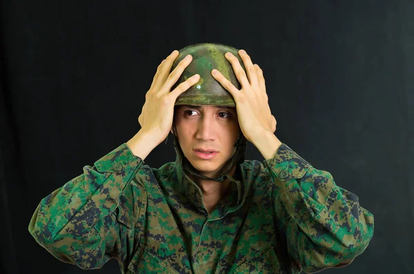 Hezký ustaraný mladý voják nosí uniformu trpí stresem rukama dotýkat jeho helmu, na černém pozadí — Stock fotografie