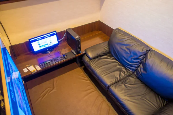 TOKYO, JAPÃO JUNHO 28 - 2017: Vista interior do local internet coffe, com um computador sobre uma mesa de madeira e um sofá preto em uma pequena sala, localizada em Tóquio — Fotografia de Stock