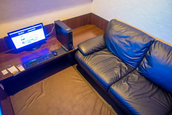 TOKYO, JAPÃO JUNHO 28 - 2017: Vista interior do local internet coffe, com um computador sobre uma mesa de madeira e um sofá preto em uma pequena sala, localizada em Tóquio — Fotografia de Stock