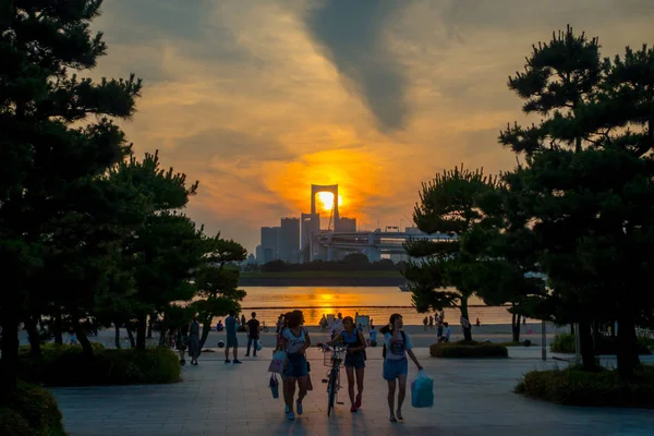 TOKIO, JAPÓN 28 DE JUNIO - 2017: Gente no identificada caminando en la playa de Odaiba al atardecer, con el puente de Osaiba en el horizonte, Tokio Japón — Foto de Stock