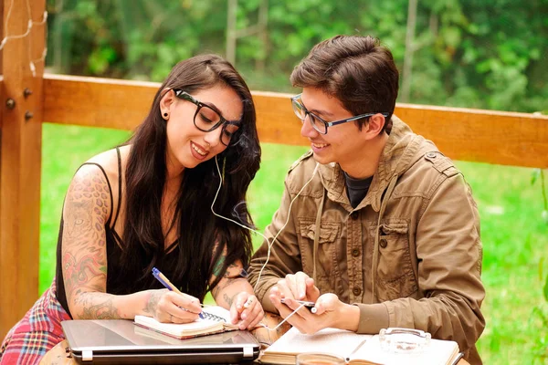 Hipster paar muziek luisteren en werken op veranda van houten huis, schrijft vrouw in een notebook terwijl man is op zoek en haar in een achtertuin achtergrond — Stockfoto