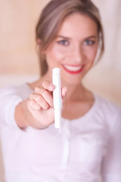 Jonge mooie lachende vrouw wijzen voor haar een menstruatie katoen tampon, in een onscherpe achtergrond — Stockfoto