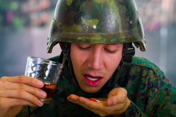 Schöner junger Soldat in Uniform, der unter dem Stress der Nachkriegszeit leidet, in der Hand ein Glas Ran und Tabletten, vor verschwommenem Hintergrund — Stockfoto