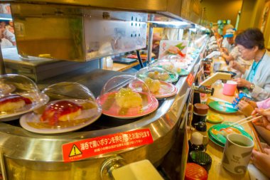 Tokyo, Japonya -28 Haziran 2017: kimliği belirsiz kişi üzerinde bir tablonun içine bir kaitenzushi Konveyör bant suşi lokantasında bir çeşitli japanesse yemek yeme. Tüketiciler kazık kadar renkli boş ne zaman tabaklar onlar 