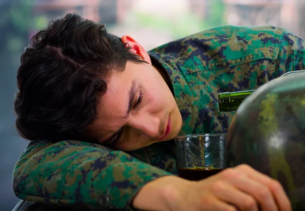 Mladý hezký spánek voják nosí uniformu trpí stresem po válce, držel v ruce sklenku ron, rozostřené pozadí — Stock fotografie