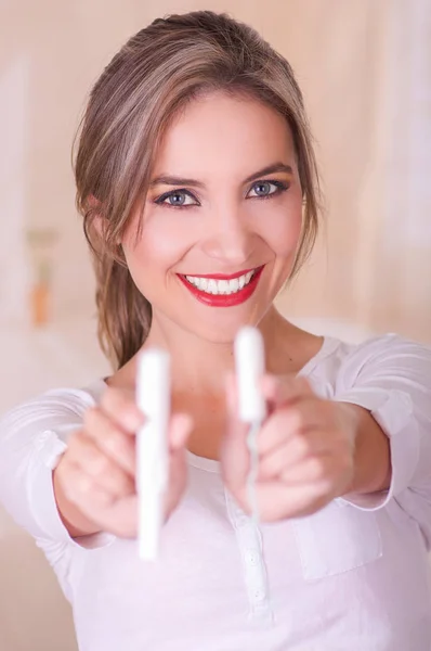 Young beautiful smiling woman pointing in front of her two menstruation cotton tampons in a blurred background — Stock Photo, Image