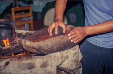 İnsanlar bir odun sobası yanındaki bir taş üzerine kakao çekirdekleri taşlama