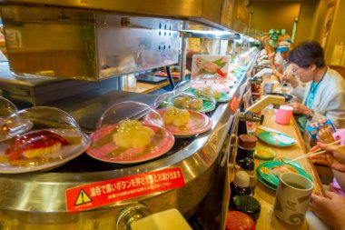 Tokyo, Japonya -28 Haziran 2017: kimliği belirsiz kişi üzerinde bir tablonun içine bir kaitenzushi Konveyör bant suşi lokantasında bir çeşitli japanesse yemek yeme. Tüketiciler kazık kadar renkli boş ne zaman tabaklar onlar 
