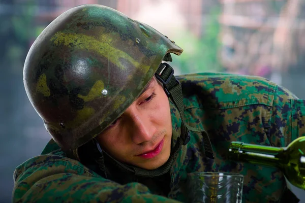 Красивий молодий солдат у формі, що страждає від стресу після війни, наповнює склянку пляшкою, на розмитому фоні — стокове фото