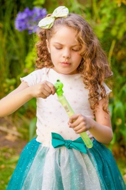 Bulanık doğa arka planda elbise giyen bir mavi kulakları kaplan aksesuarları kafasını ve bir prenses üzerinde yaz niteliğine sabun köpüğü ile oynarken küçük kıvırcık kız mutlu