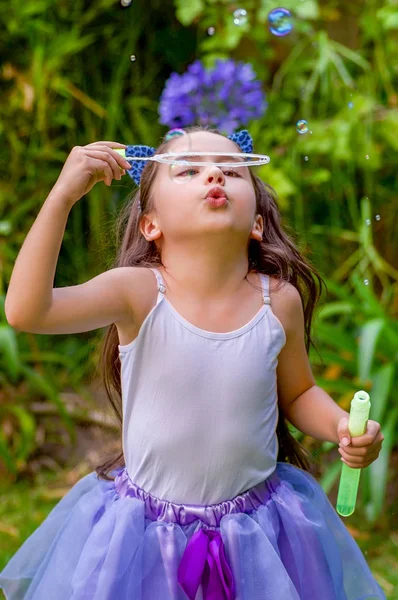 Happy little girl playing with soap bubbles on a summer nature, wearing a blue ears tiger accessories over her head and a princess dress in a blurred nature background — Stock Photo, Image