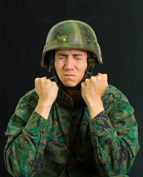 Pohledný mladý voják nosí uniformu trpí stresem, zvrásnění obličej oběma rukama dělá pěstí, na černém pozadí — Stock fotografie