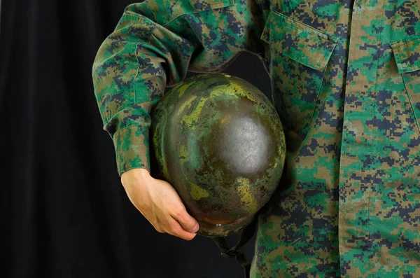 Joven soldado vistiendo uniforme, y sosteniendo bajo su brazo el casco, en un fondo negro — Foto de Stock