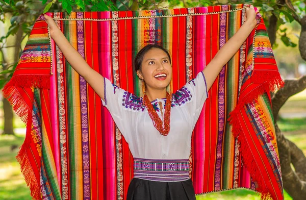 QUITO, ECUADOR - 30 DE AGOSTO DE 2017: Una joven indígena no identificada vistiendo una típica ropa andina, sosteniendo con ambas manos una manta colorida en el parque — Foto de Stock
