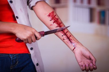 Genç bir depresif kadın elinde bir bıçakla kolunu kanama, bulanık bir arka plan ile yakın çekim