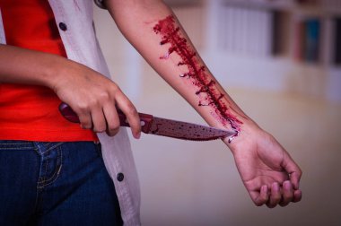 Genç bir depresif kadın elinde bir bıçakla kolunu kanama, bulanık bir arka plan ile yakın çekim