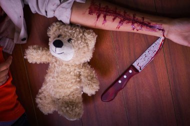 Genç bir depresif kadın elinde bir bıçakla, kanama, ahşap bir arka planda yanında, bir oyuncak ayı ile kolu ile yakın çekim