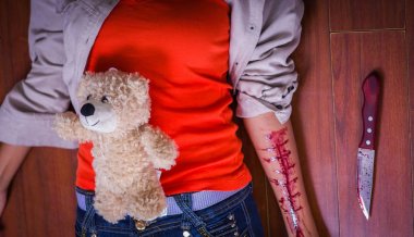 Onun kol, bir oyuncak ayı karnı ve ahşap arka plan yanında, bir bıçak ile kanama genç bir depresif kadın kapatmak