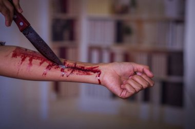 Genç bir depresif kadın elinde bir bıçakla kolunu kanama, bulanık bir arka plan ile yakın çekim