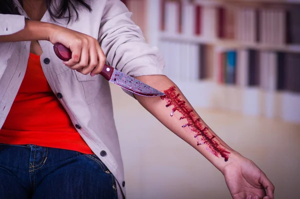 Close up de uma jovem mulher depressiva segurando uma faca com o braço sangrando, em um fundo embaçado — Fotografia de Stock