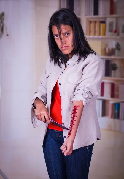 Крупный план молодого депрессивного подростка, держащего нож с рукой, истекающей кровью, на размытом фоне — стоковое фото
