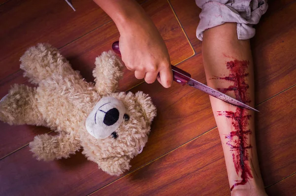 Genç bir depresif kadın elinde bir bıçakla, kanama, ahşap bir arka planda yanında, bir oyuncak ayı ile kolu ile yakın çekim