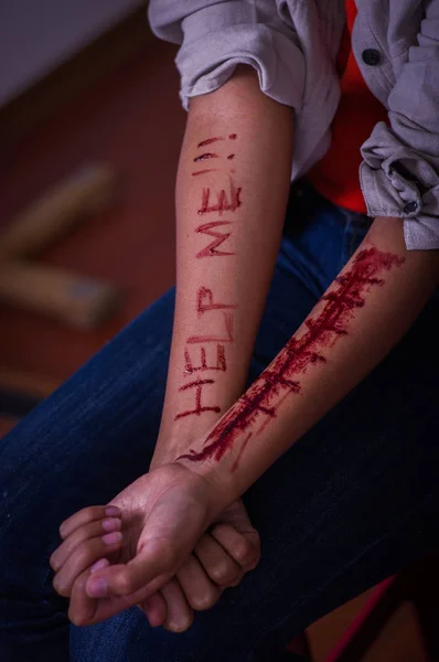 Close up of a young depressive woman, with both arms bleeding with the help word written in her arm with a knife, in a blurred background — Stock Photo, Image