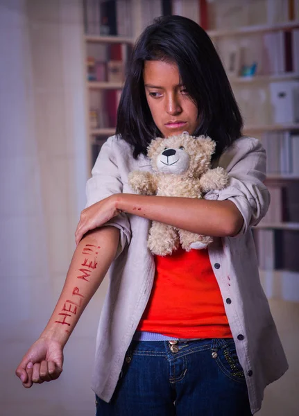 Close up of a young depressive woman with her arm bleeding, hugging a teddy bear, in a blurred background — Stock Photo, Image