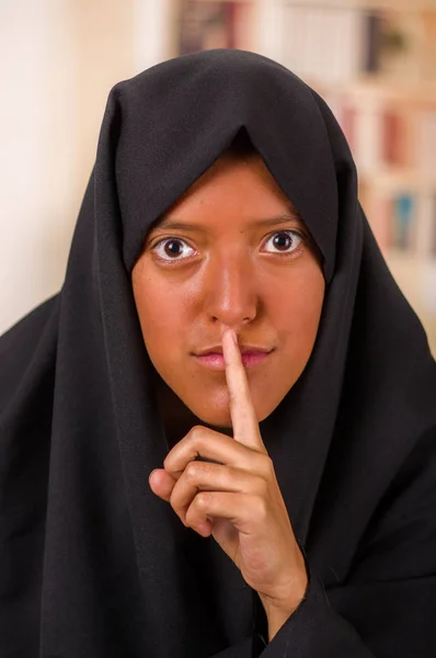 Retrato de una hermosa chica musulmana usando un hiyab, y haciendo un signo de silencio con su mano, en un fondo borroso — Foto de Stock