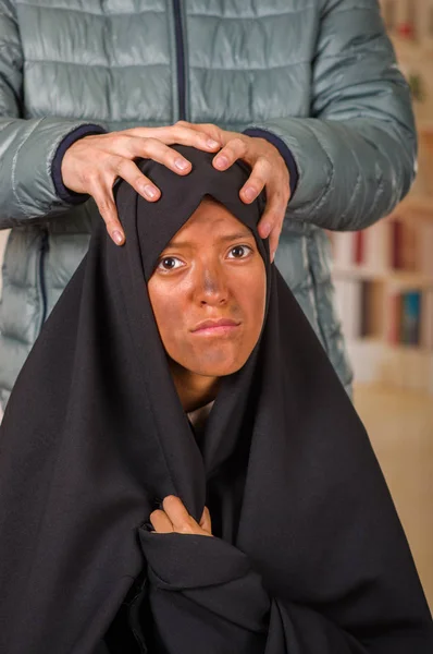 Πορτρέτο του μια μουσουλμανική κορίτσι που φορούσε ένα hijab, με ένα λευκό άνδρα πίσω από τη χρήση της και τα δύο χέρια καταπιέζει το κεφάλι της, σε ένα θολή φόντο — Φωτογραφία Αρχείου