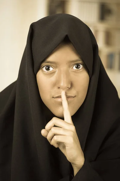 Porträtt av en vacker muslimsk tjej bära en hijab, och gör en tystnad logga med hennes hand, i en suddig bakgrund — Stockfoto
