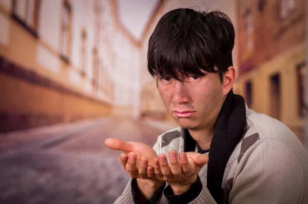 Porträt eines obdachlosen jungen Mannes auf der Straße, der mit beiden Händen Geld fordert, vor verschwommenem Hintergrund — Stockfoto