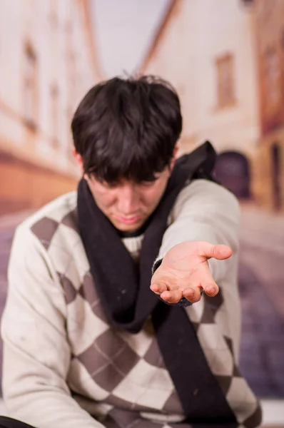 Acercamiento de un joven sin hogar en las calles, pidiendo dinero con una mano, en un fondo borroso — Foto de Stock