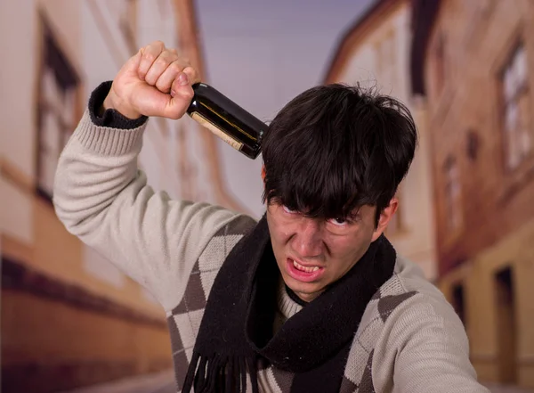 Portrét rozzlobený bezdomovci mladíka v ulicích, s lahví vína v ruce, rozostřené pozadí — Stock fotografie
