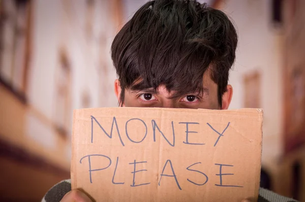 Retrato de un vagabundo con descripción de cartón del dinero por favor, escondiendo la mitad de su cara, en un fondo borroso — Foto de Stock