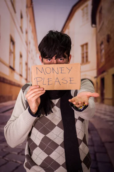 Primer plano de un vagabundo con descripción de cartón del dinero por favor, escondiendo la mitad de su cara, en un fondo borroso — Foto de Stock
