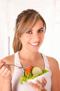 Beyaz bir t-shirt giyen ve sağlıklı bir salata elinde tutan güzel genç kadın