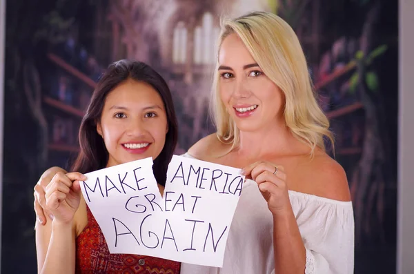 Zwei junge Frauen blonde und lateinamerikanische Mädchen lächelnd und Rassismus Idiosynkrasie von einer amerikanischen Person und fremden Menschen brechen, zerstören ein Papier, das geschrieben wird machen Amerika wieder groß, Rassismus, Gewalt — Stockfoto